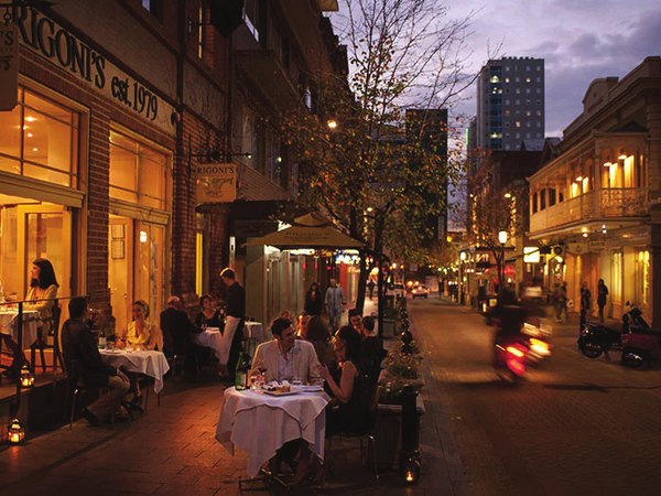 Diners at outdoor tables on a lamp-lit laneway at dusk.