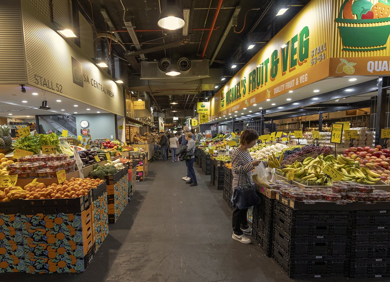 Fruit and vegetable stalls lining an aisle of the Adelaide Central Market.